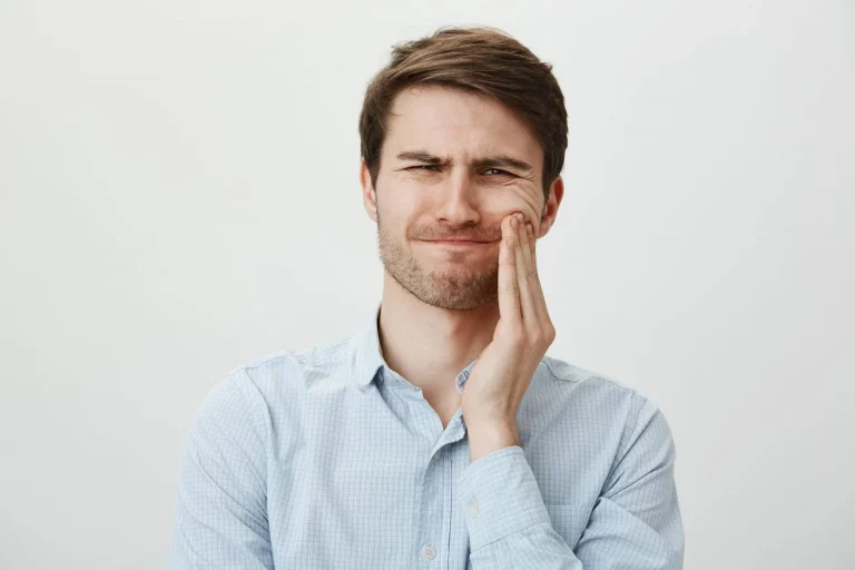 Mann fasst sich an den Kiefer und zeigt Beschwerden im Kiefergelenk als Symbolbild für CMD und Kieferschmerzen