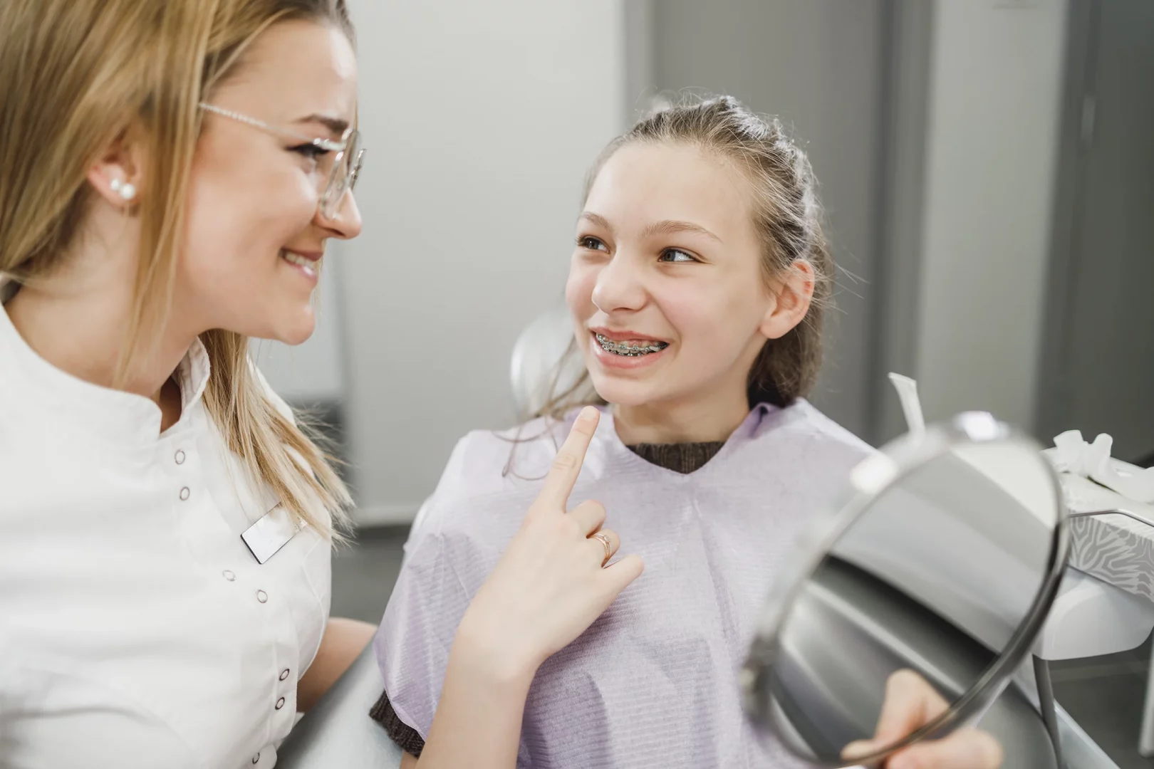 Jugendliche Patientin nach dem Einsetzen einer festen Zahnspange mit Metallbrackets beim Beratungsgespräch in einer kieferorthopädischen Praxis.
